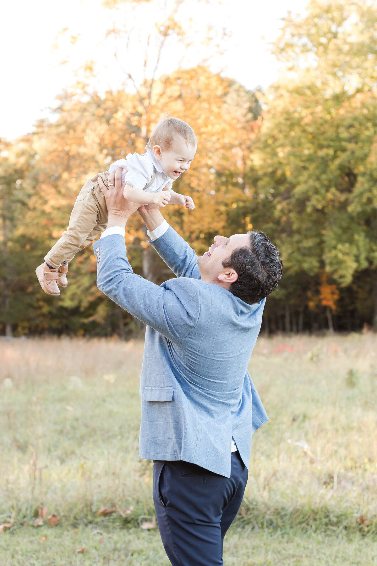 A sweet dad playing with his toddler boy by throwing him in the air outside in the Fall by DC Family Photographer