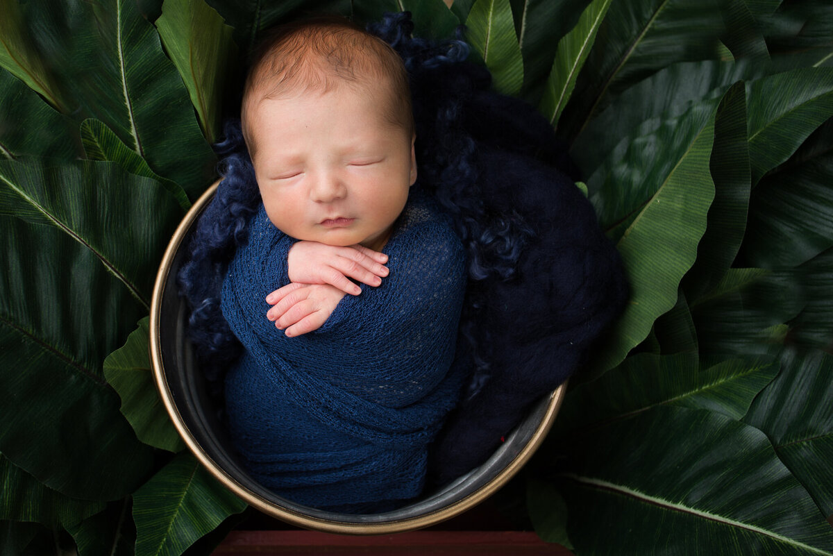Newborn nestled in a green, leaf-inspired bowl, surrounded by tropical foliage. Captured in Overland Park, Kansas, this vibrant setup is perfect for families seeking nature-themed newborn photography.