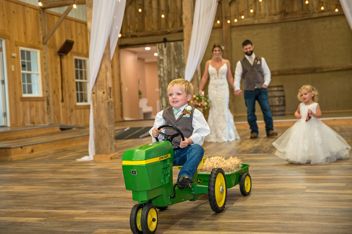 Wedding ring bearer driving tractor entering reception venue.
