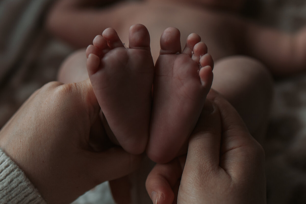 Een persoon houdt de kleine voetjes van een baby vast, wat een moment van tederheid en zorgzaamheid uitstraalt.