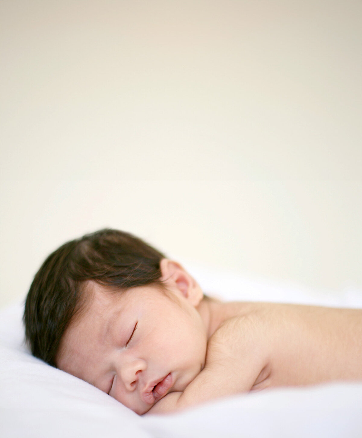 San Francisco newborn photographer captures natural, unposed portrait of sleeping baby with dark hair on white blanket, no props, in soft natural light.