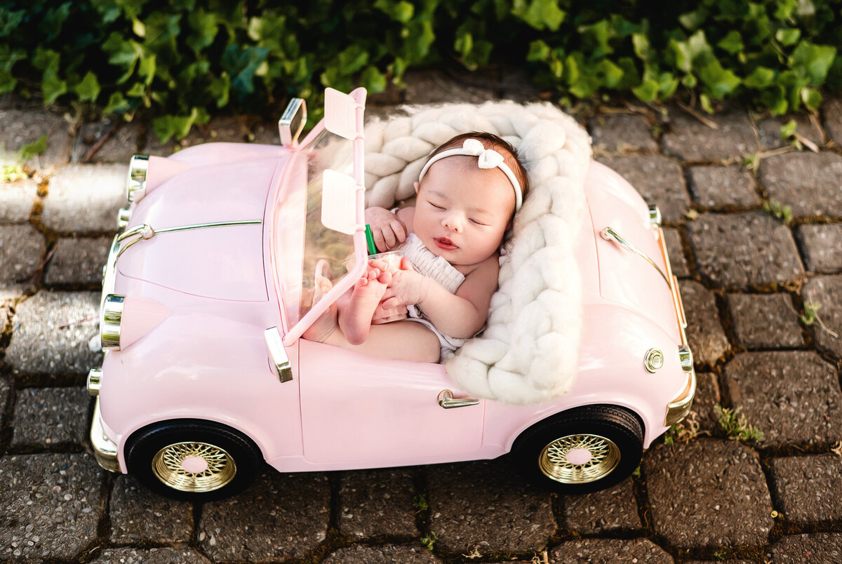 Tiny infant girl sleeping in a pink car at her newborn photoshoot in Greater Toronto.