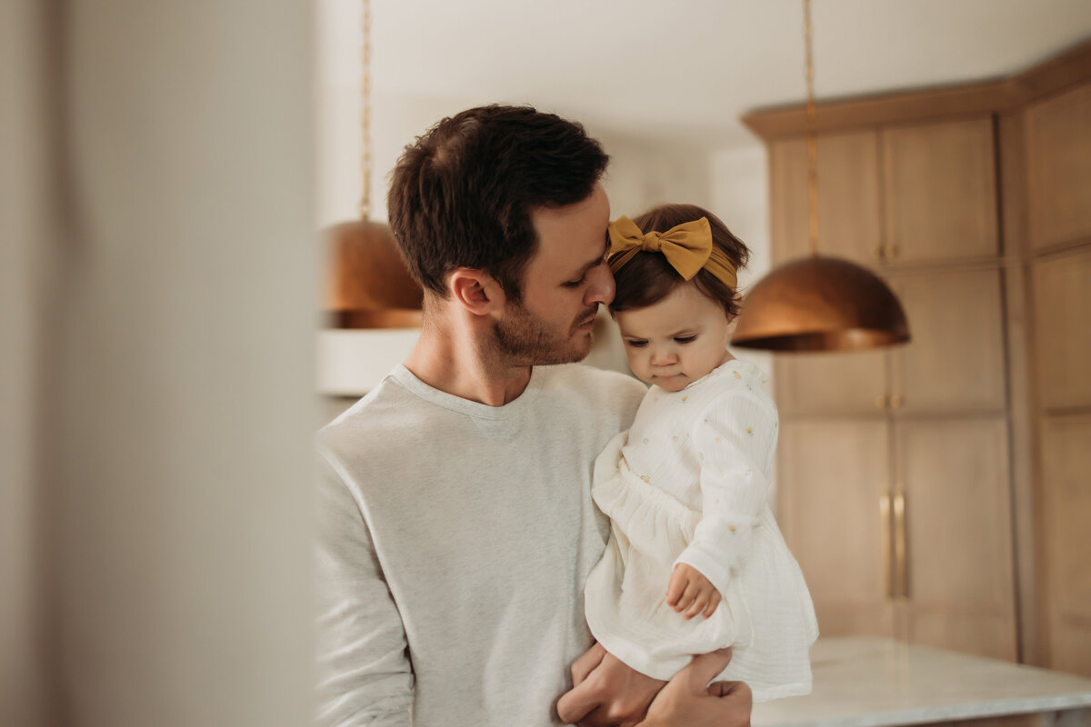 Dad holds toddler daughter while kissing her on the cheek