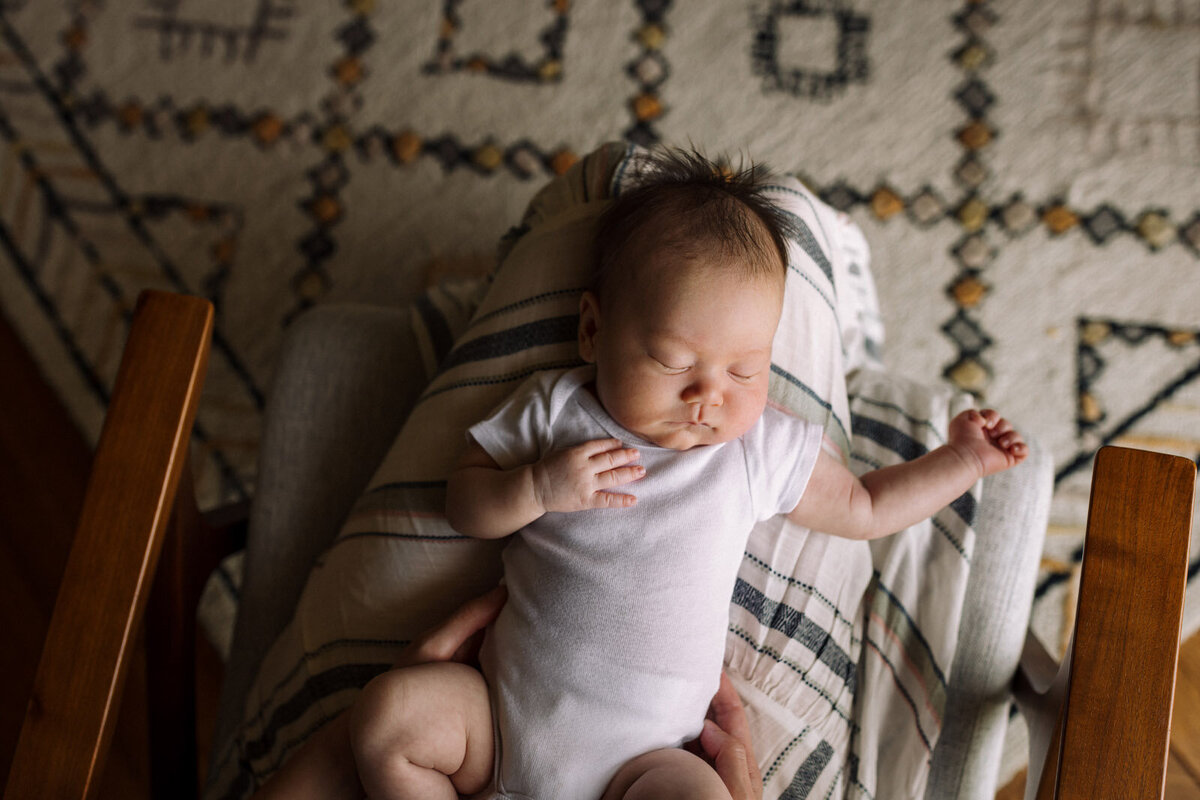 newborn in white onesie sleeping on mom's lap above patterned rug