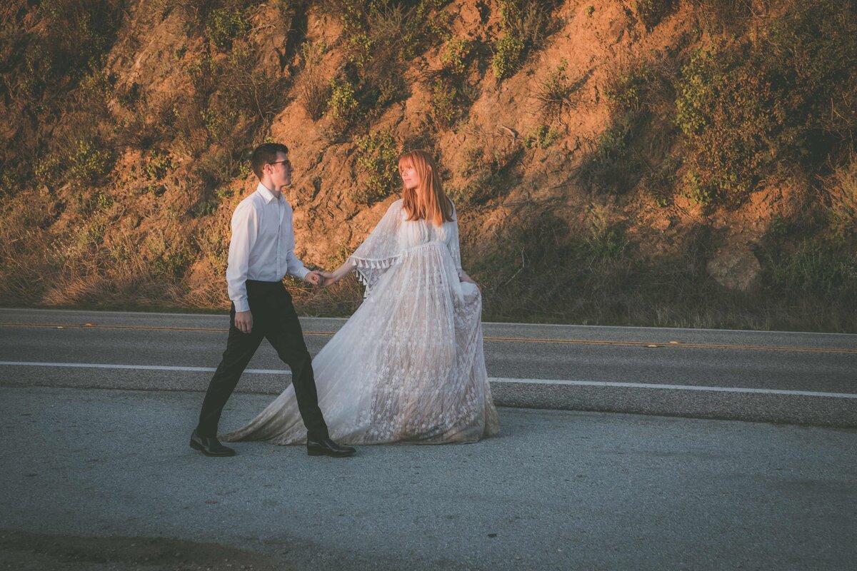 Bride and groom holds hands while walking down Highway 1.