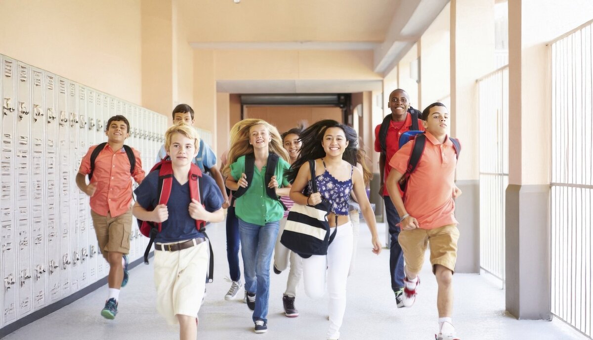 Excited students running down a school hallway with backpacks on