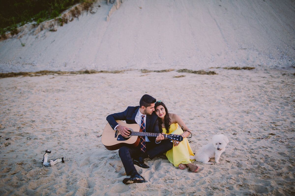 Couple playing the guitar at the callahans beach for his fiance with their puppy dog