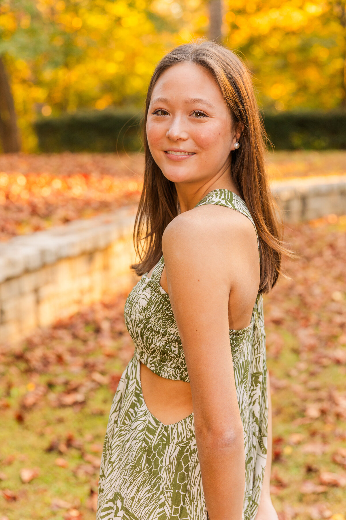 senior girl looking at the camera over her shoulder wearing a summer green and white dress during portrait photo session