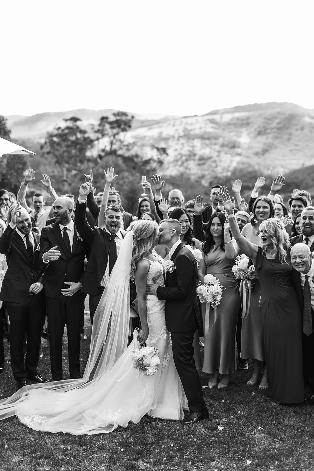 Bride and groom kiss in front of their family while they cheer