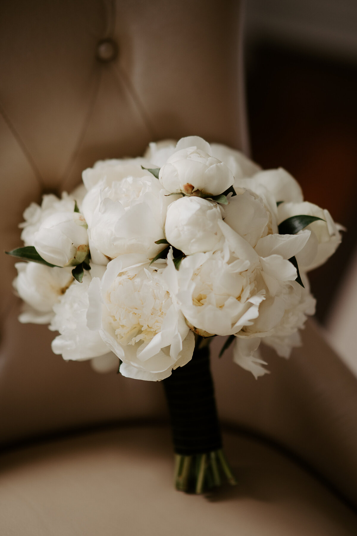A modern bouquet of white peonies sitting on a brown leather chair at a Montreal wedding. 