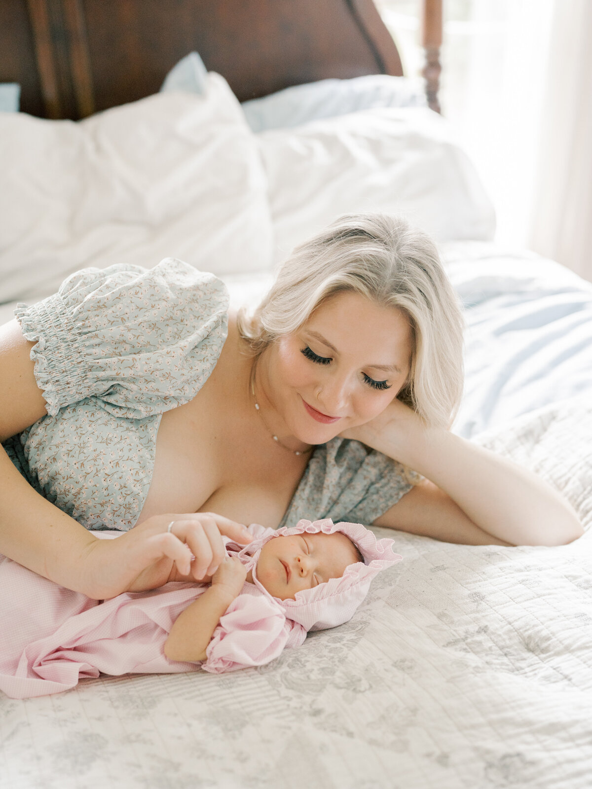 Mom laying with newborn baby on bed while baby is wearing a bonnet in Williamsburg Virginia