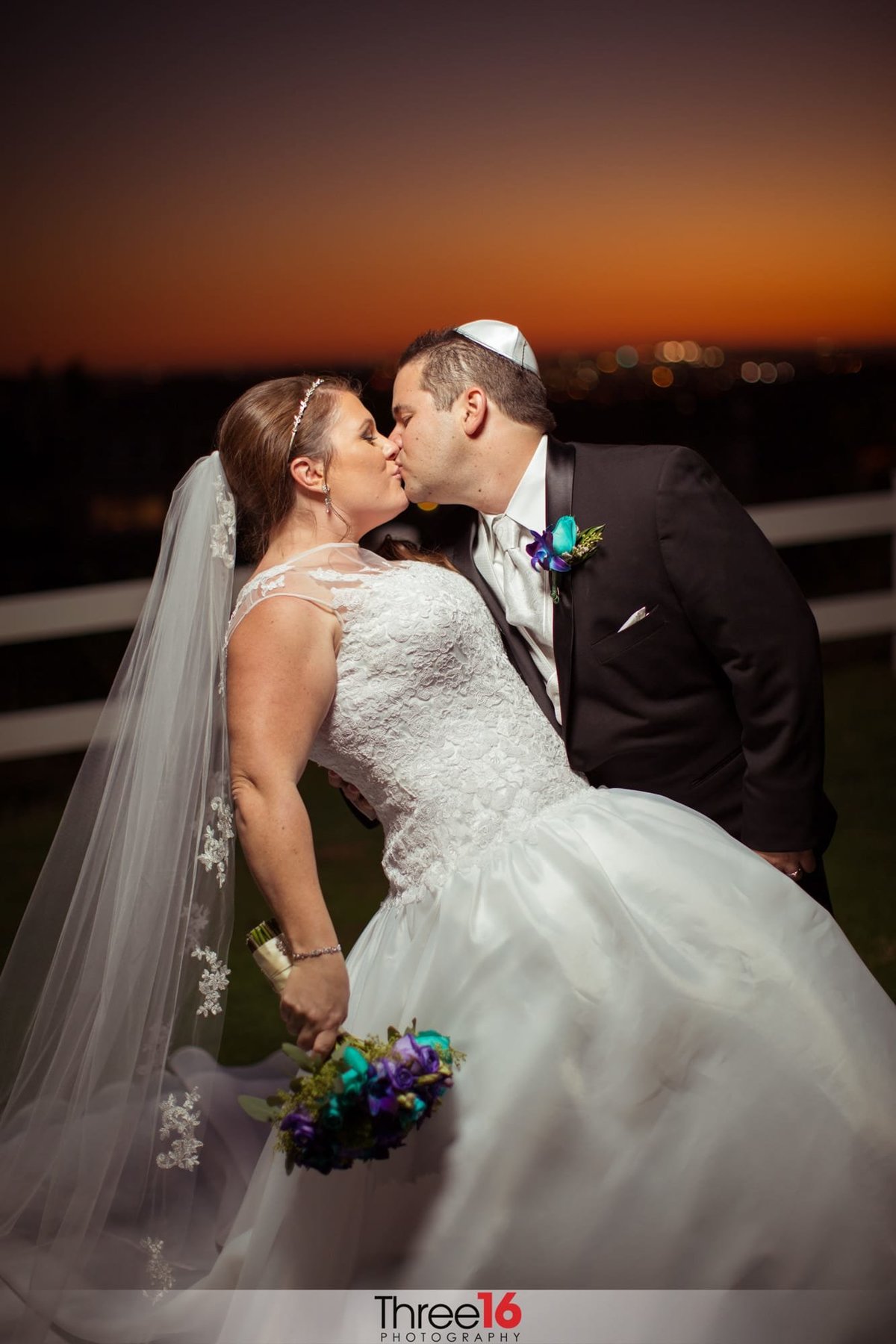 Groom dips his Bride and kisses her during photo session with a beautiful sunset in the background