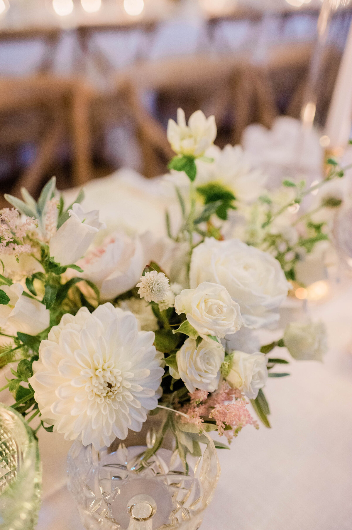A close-up of a floral arrangement with soft white roses, dahlias, and lush greenery at a reception table.