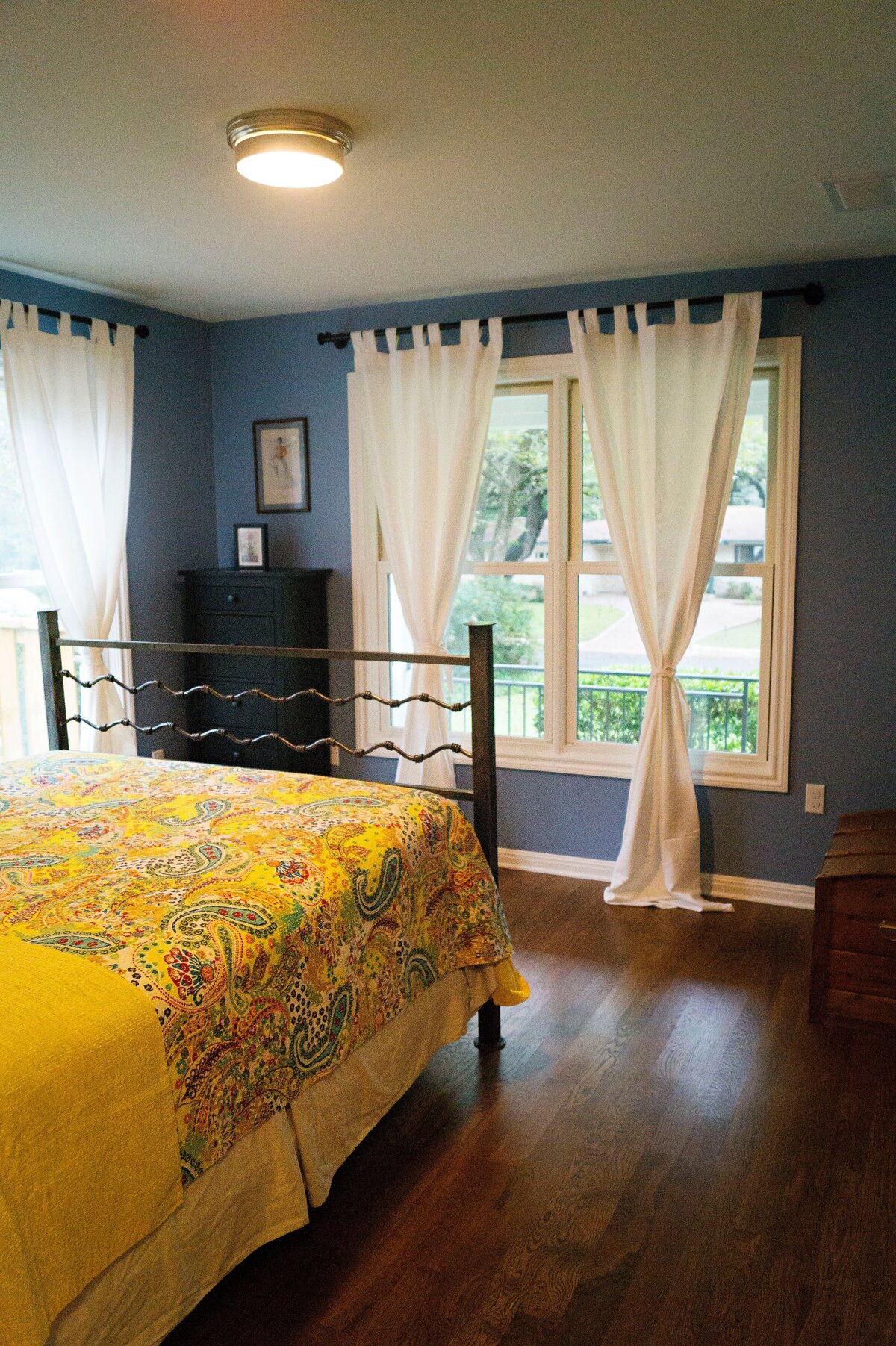 cozy bedroom in austin, texas with dark hardwood floors and white drapes.