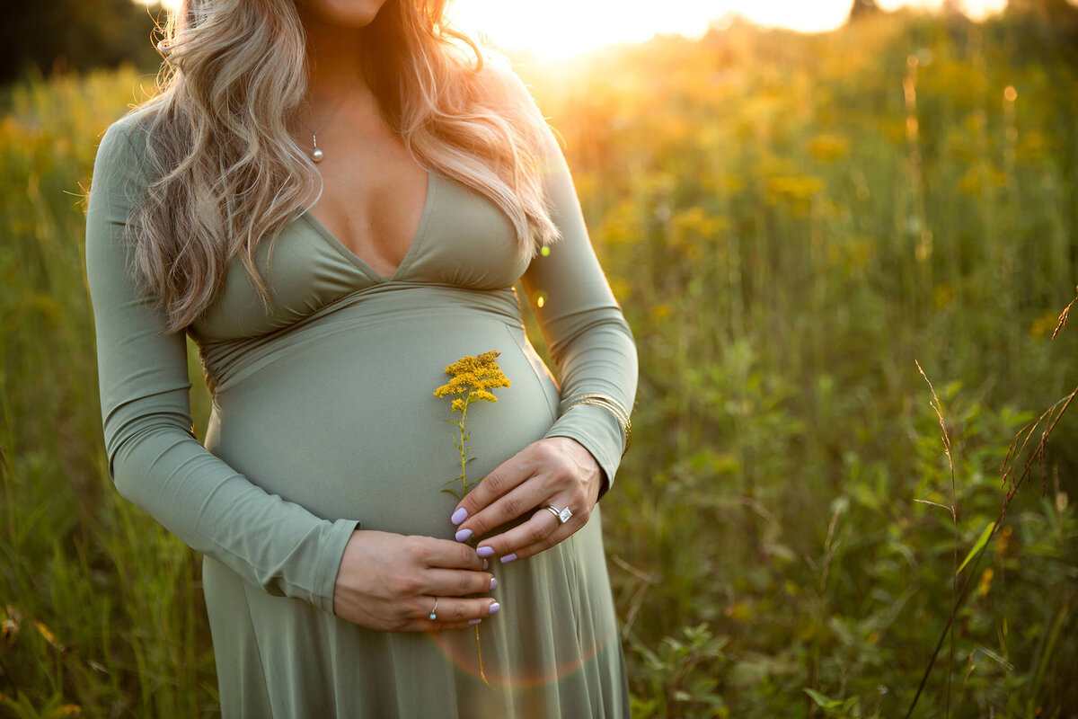 Pregnant mom in green dress with yellow flower in a field