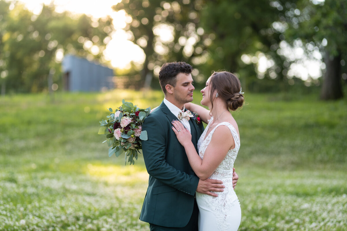 Bride and groom embrace while holding bouquet in a field