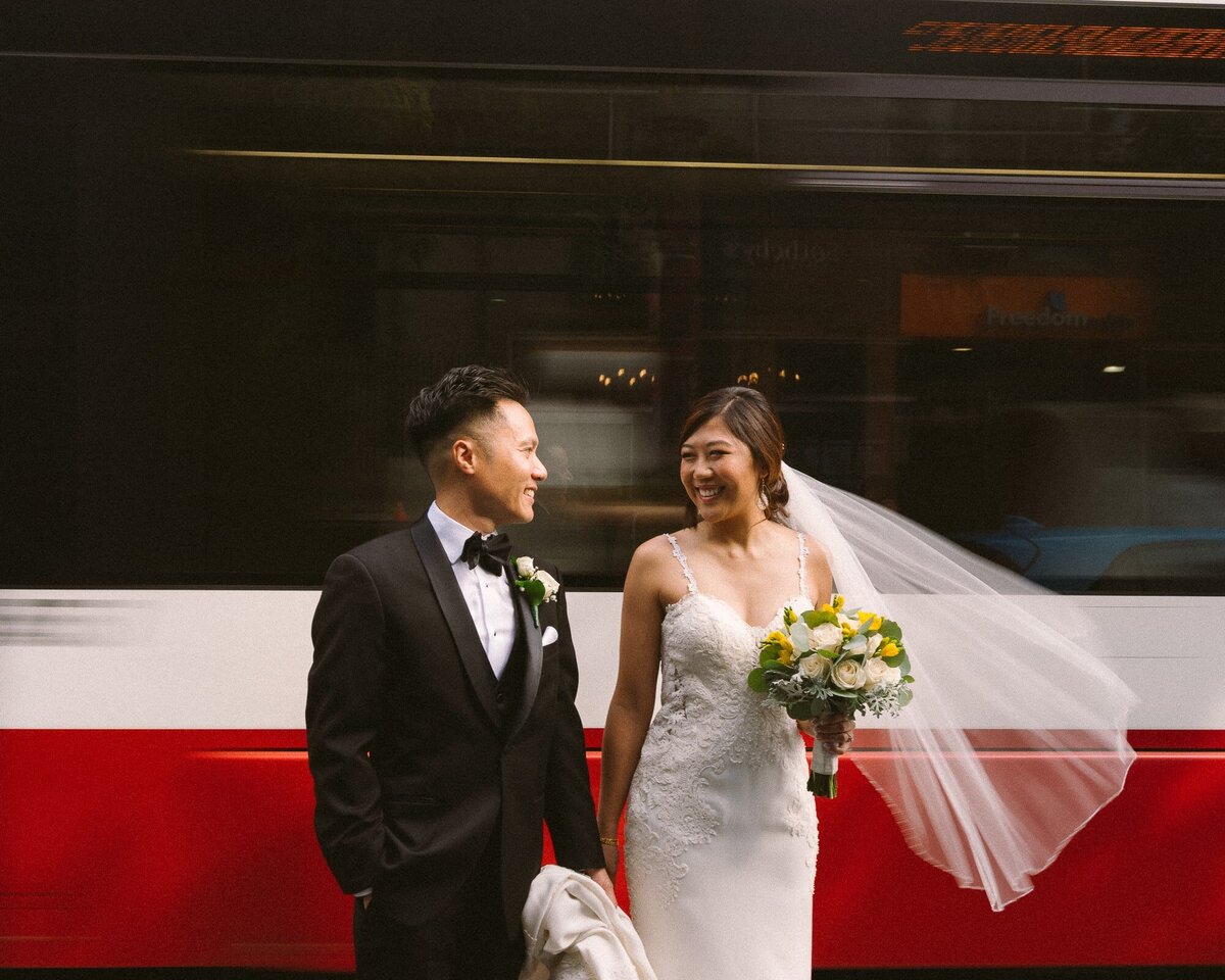 bride and groom holding hands as streetcar passes by behind them
