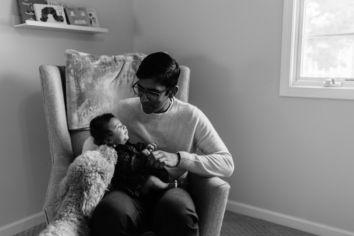 indian dad holding newborn daughter while golden doodle sniffs at her