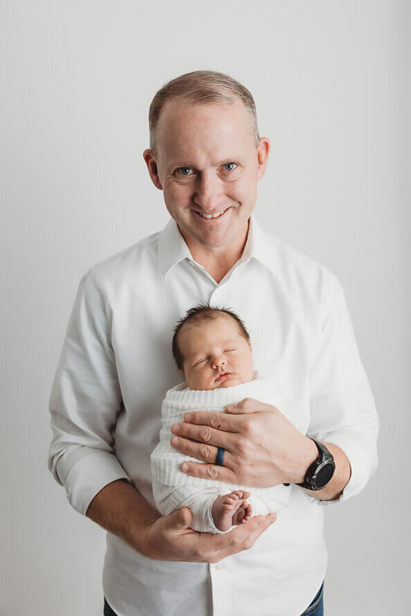 Dad holds his newborn baby in the studio at Angela Marie Media.