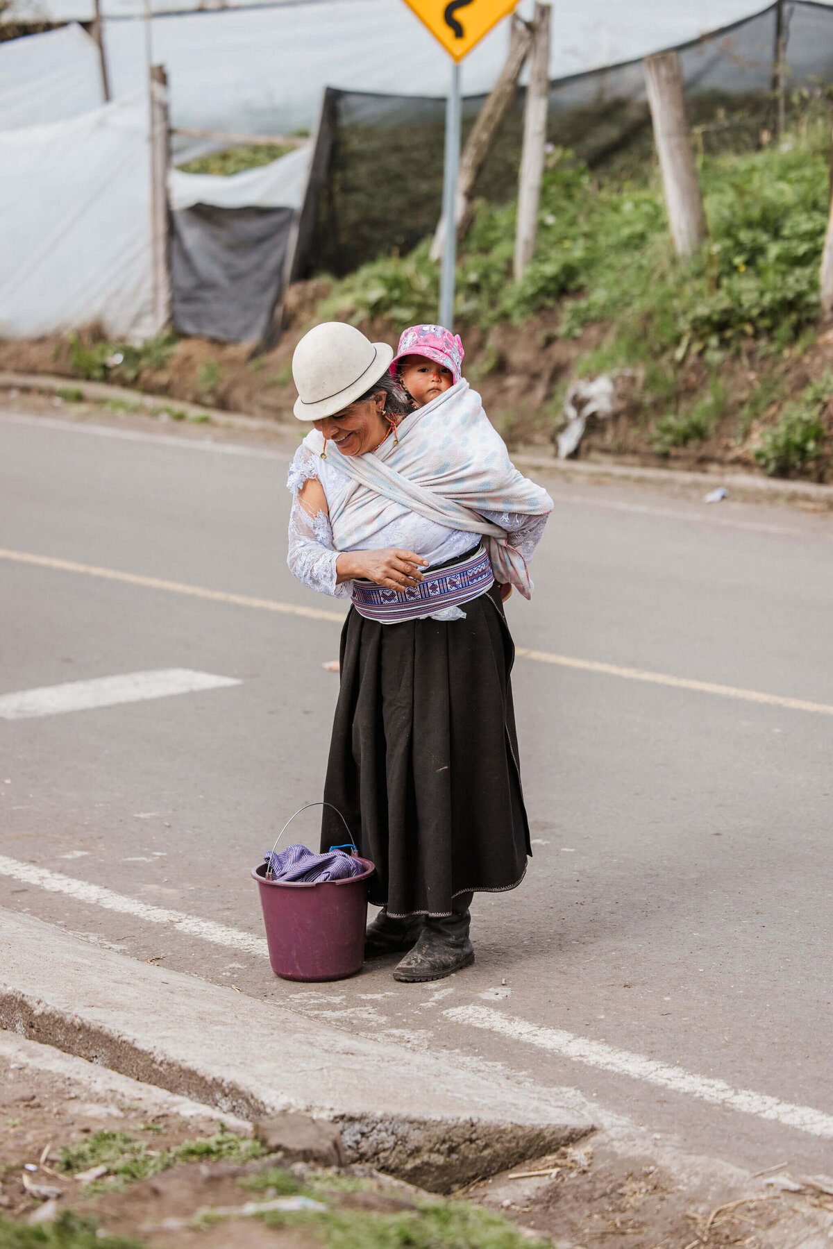 Lady standing in the streets of Ecuador with small child on back