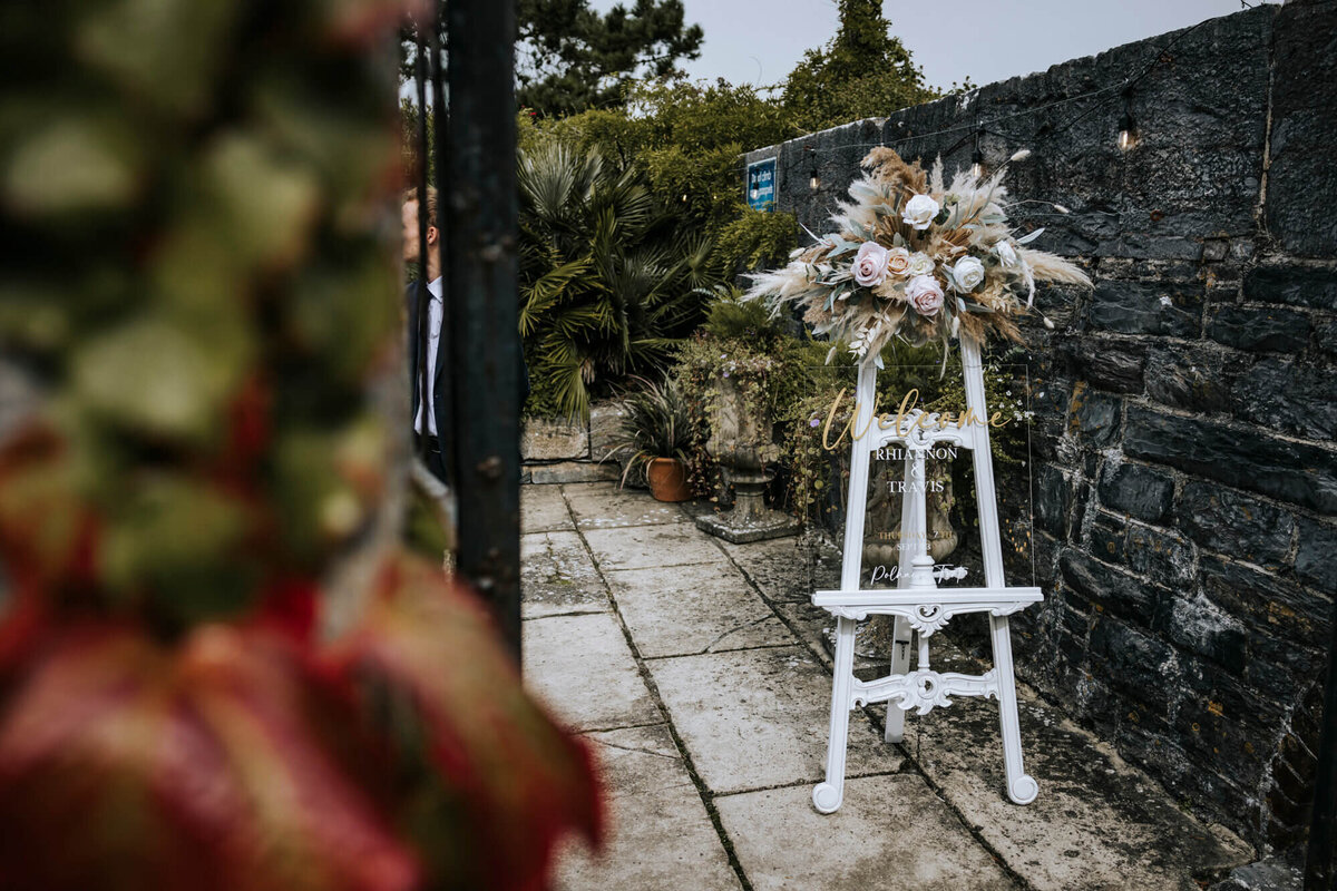 A white easel decorated with flowers with a clear acrylic sign