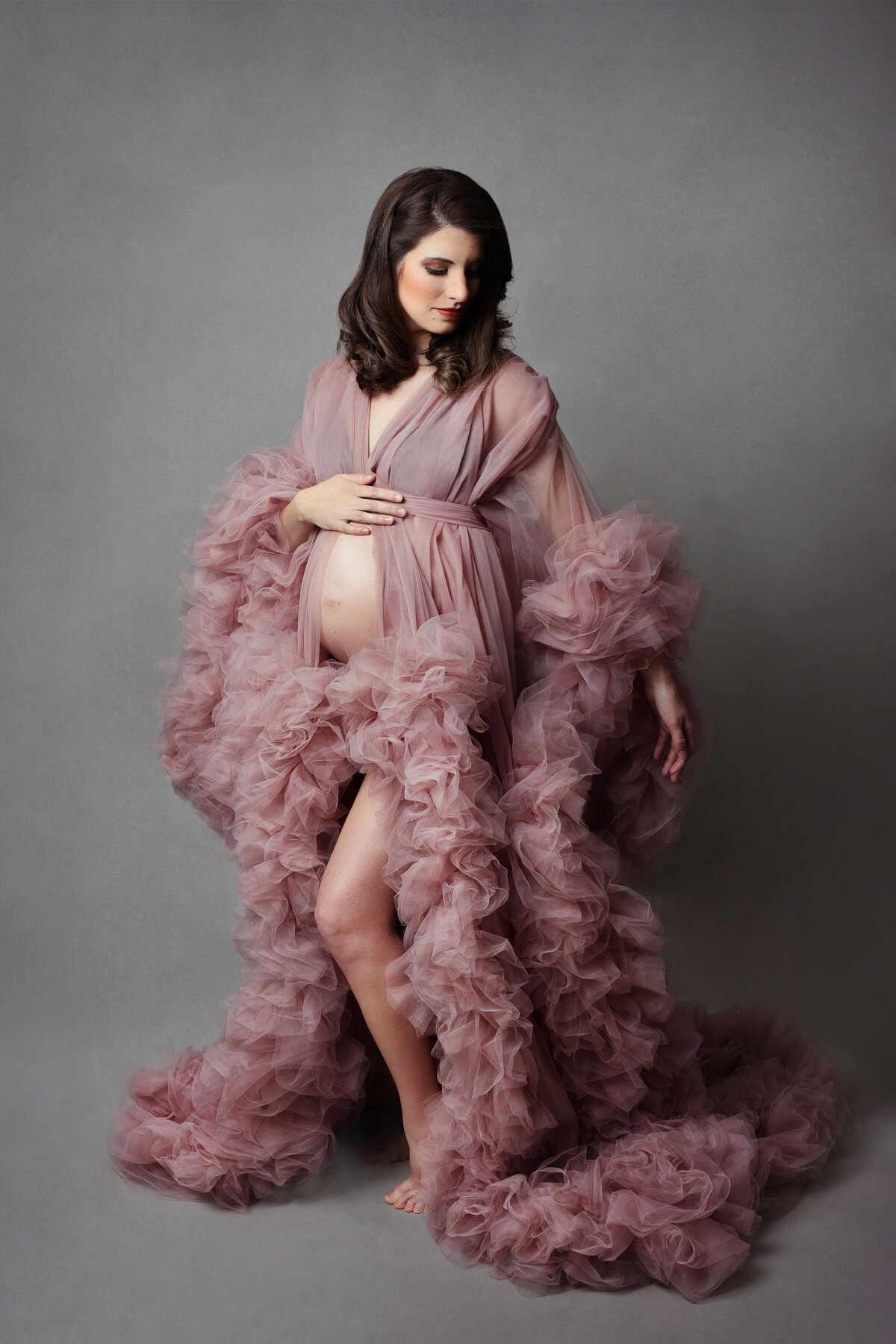 pregnant mother wearing a pink maternity gown/robe at her maternity photo shoot at a maternity photography studio