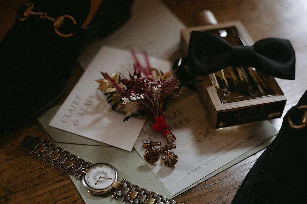 Parfum, noeud papillon, invitation, montre te bouquet de fleurs séchées soigneusement disposés sur une table en bois. Photo par kamescop, photographe de mariage vintage, Bretagne et ailleurs.