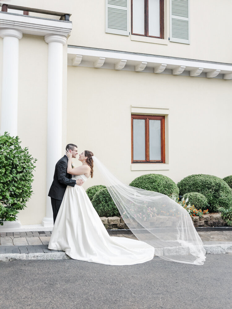 bride and groom kissing as veil blows in the wind