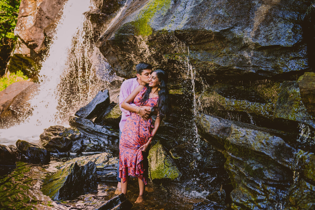 Groom kissing bride during their engagement session near a waterfall at the Devil's hopyard in Connecticut