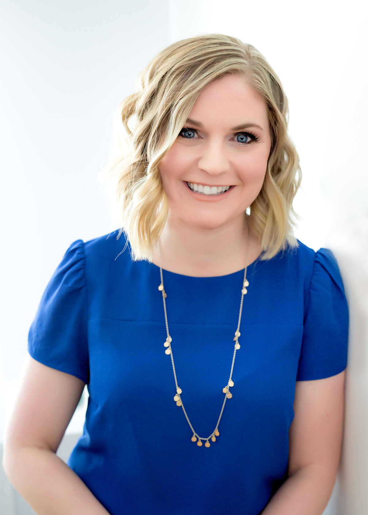 Female headshot client wearing a bright blue top, facing straight-on to the camera, smiling