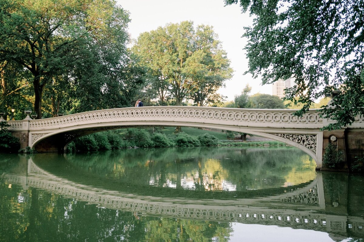 an engaged couple standing on Bow Bridge in Central Park