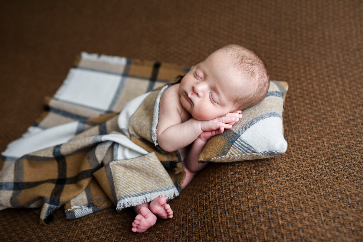 newborn baby lying down covered with a brown and white plaid blanket for newborn photos
