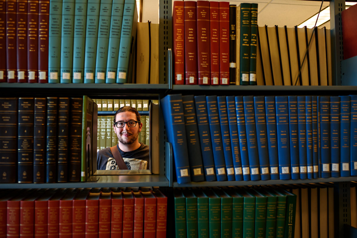 Portrait of a college student in a library framed by books.