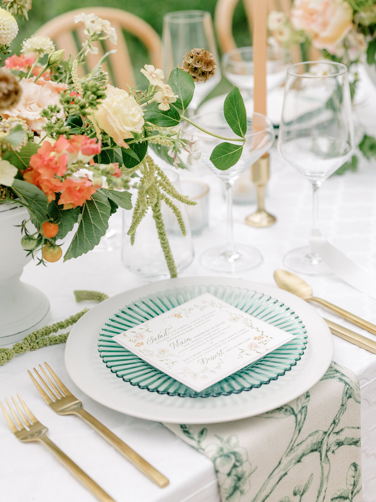 Photo of a wedding reception place setting with a cream and green napkin under a white charger under a green salad plate with a dinner menu on top