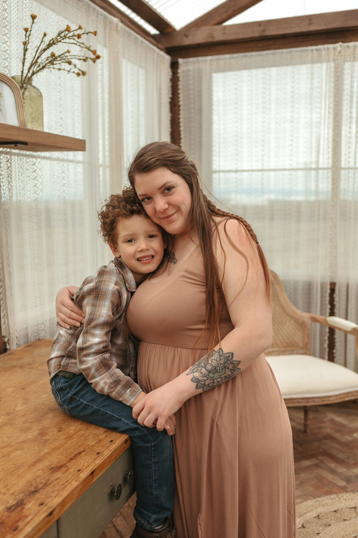 little boy in plaid shirt looking and smiling at camera while mom is hugging him in firestone colorado