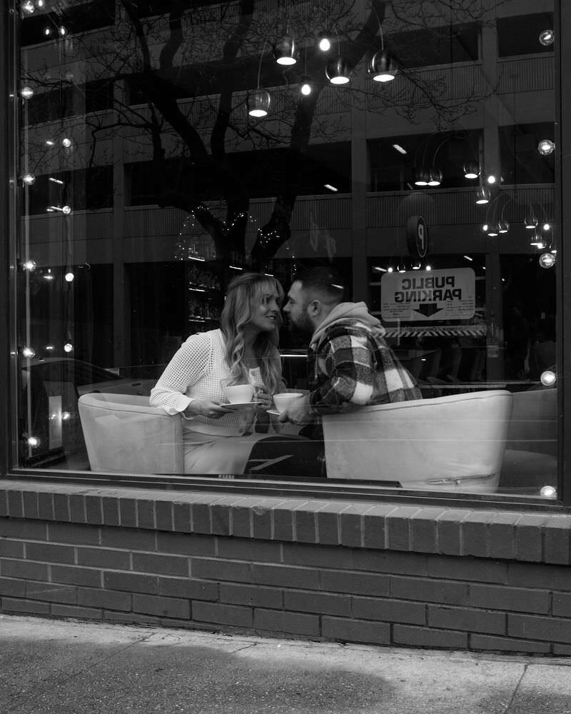 A coffee shop couple shares a romantic moment among the bookshelves during a library engagement session in Spokane, Washington.