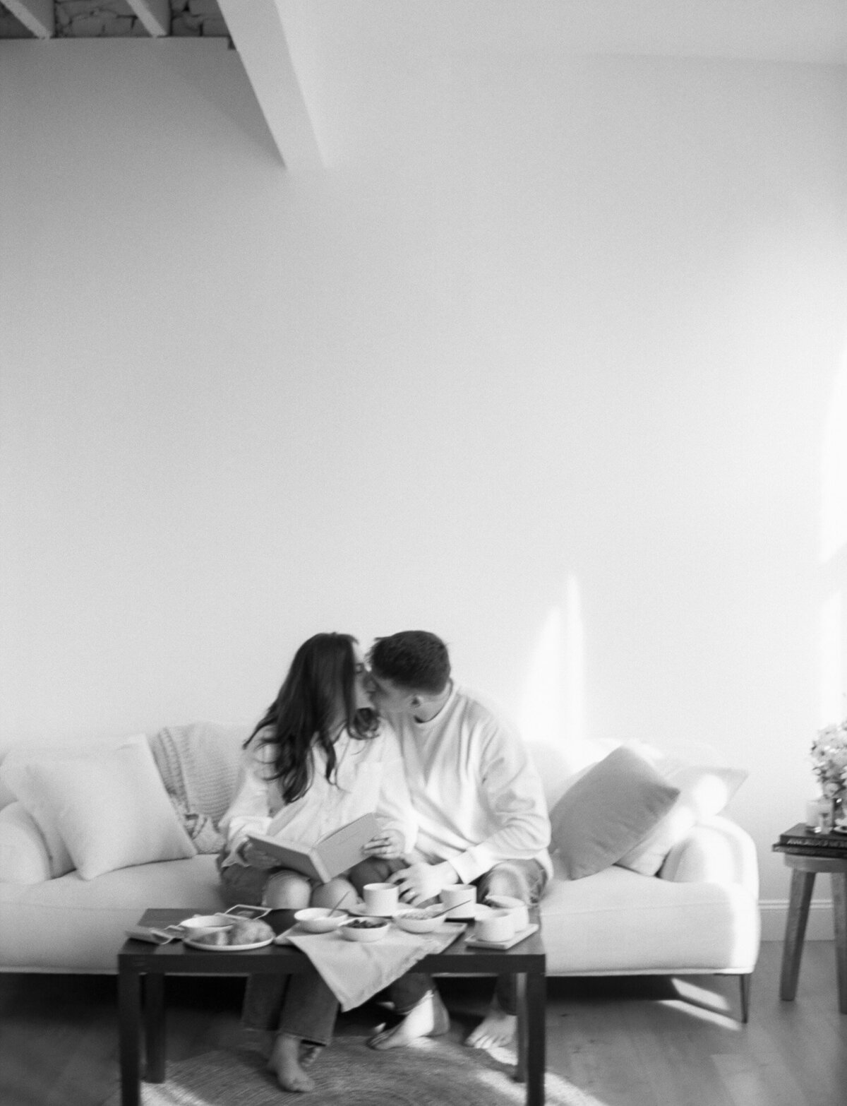 couple kisses on couch in white, natural light studio during film branding photography in Michigan