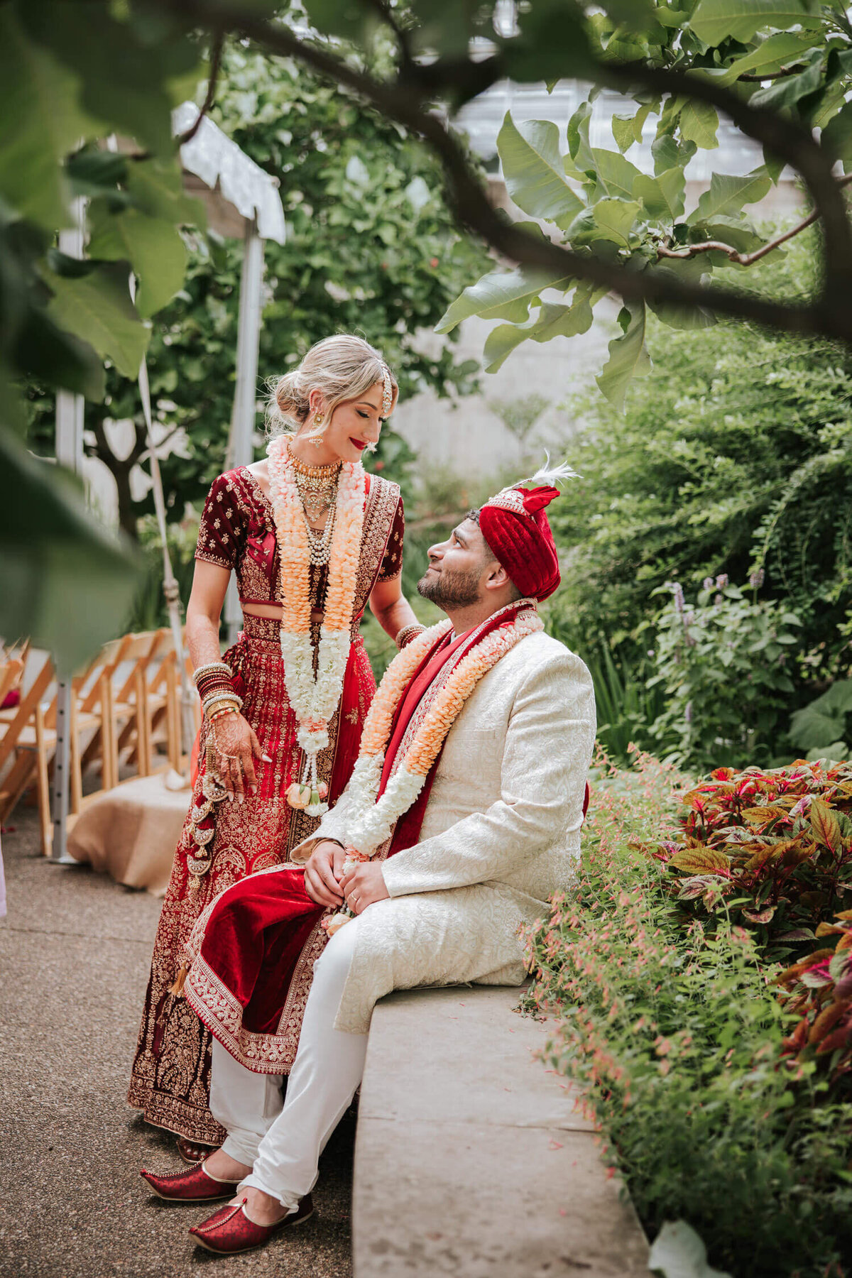 A bride and groom in traditional wedding attire share a joyful moment in a lush garden setting, at The Phipps Conservatory