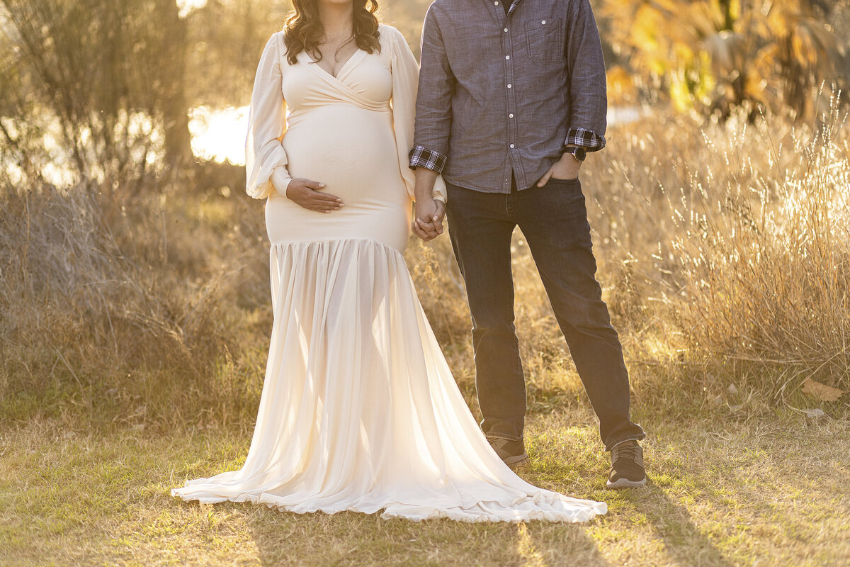 mother holding pregnant belly while holding hands with husband