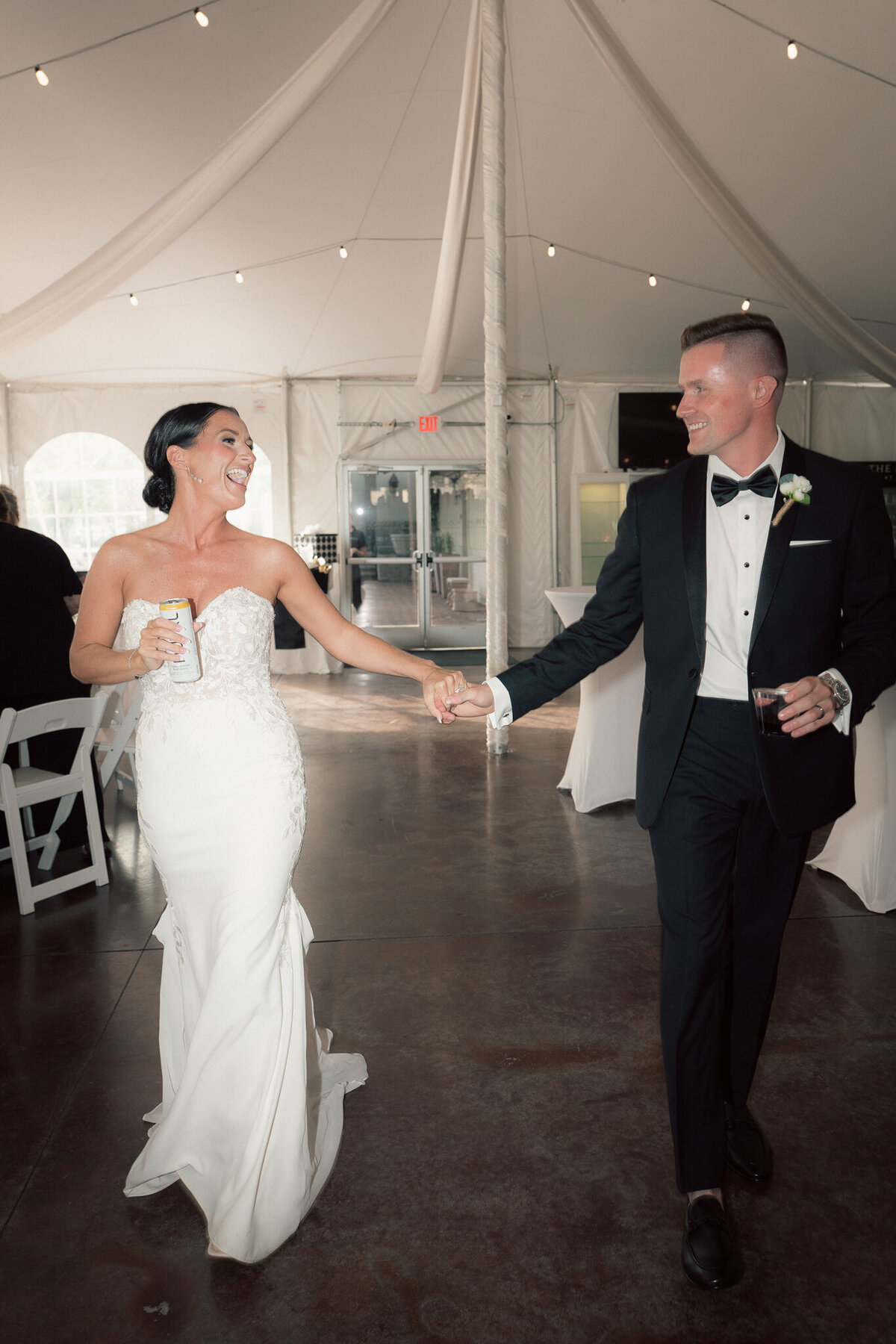 Bride and groom entering wedding reception tent holding hands joyfully