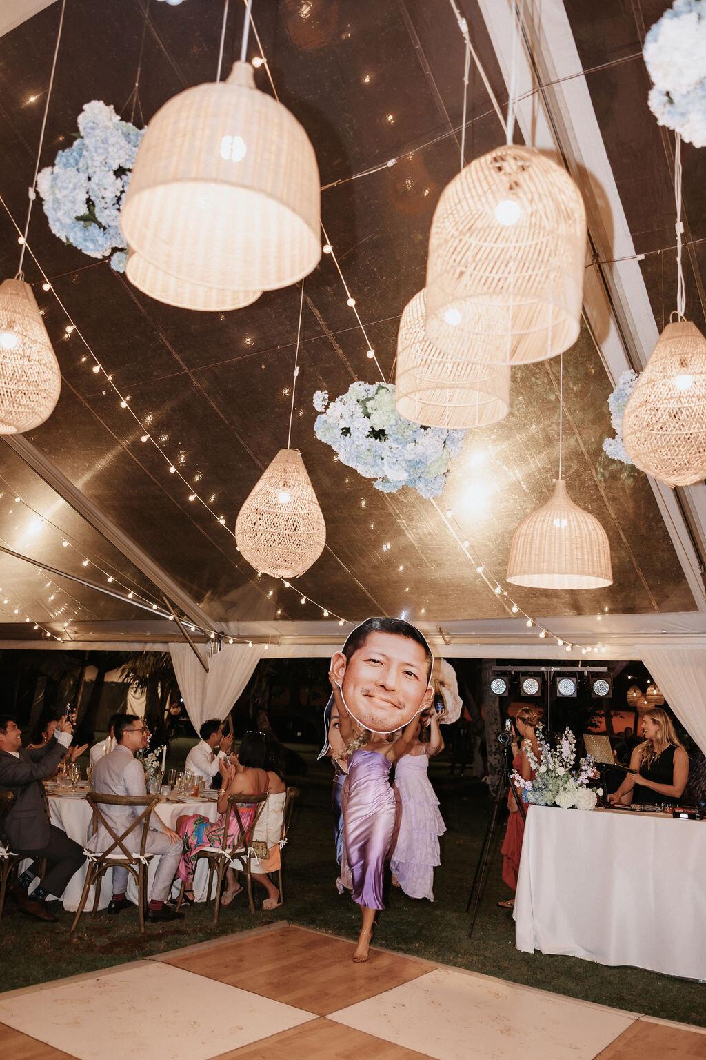 wedding reception at lanikuhonua bridesmaids entering with giant cardboard cut out of grooms face under clear tent and lantern installation