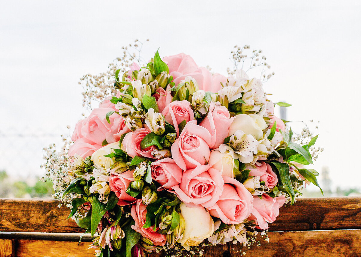 A pink and green bridal bouquet rests on a wooden table at a wedding designed by a luxury celebrity wedding planner.