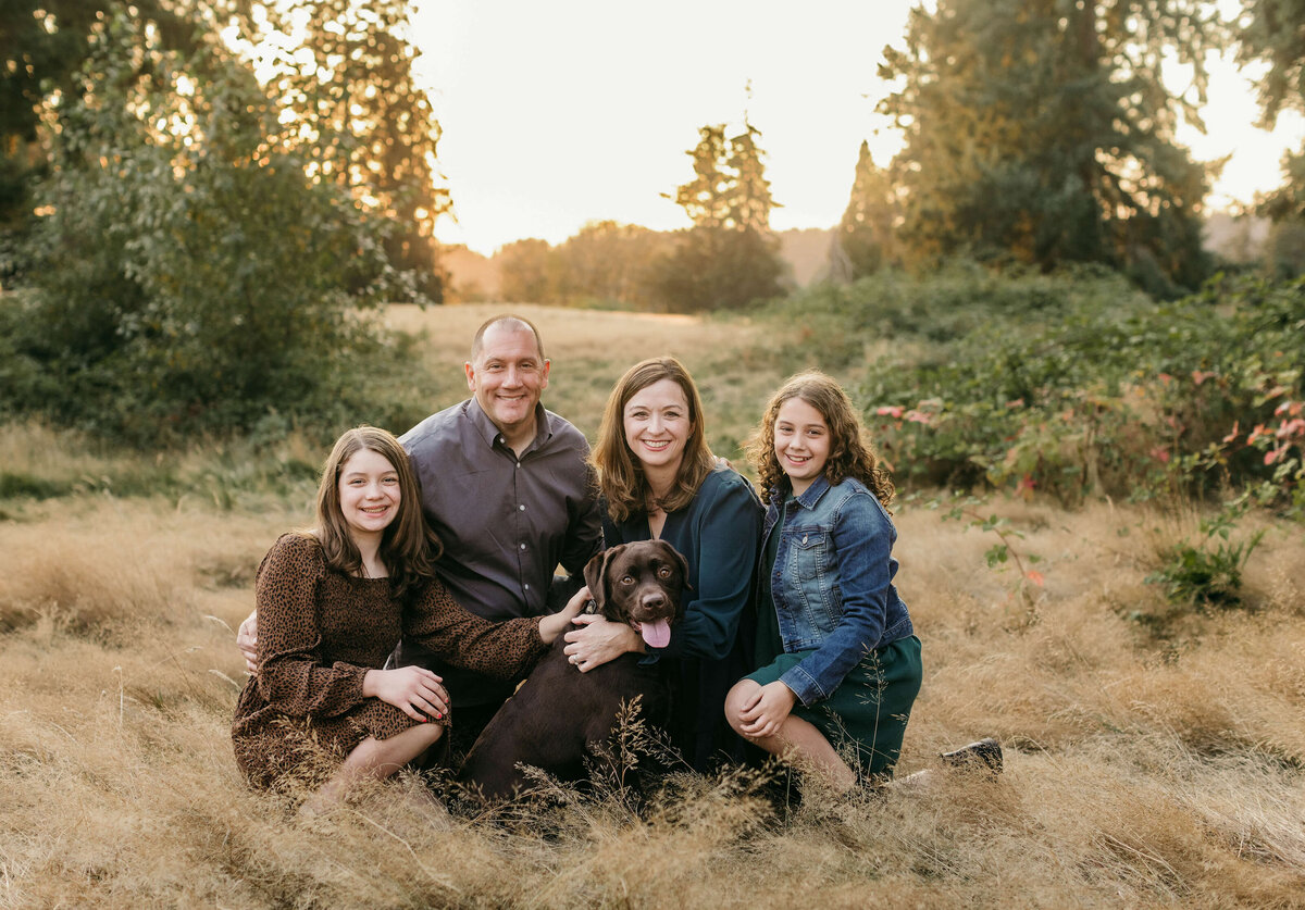 Family of 4 with their chocolate lab pup in a field of grass