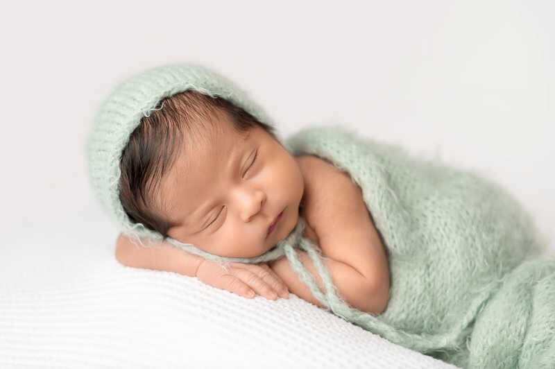 Newborn baby sleeping on side with green wrap during Houston lifestyle newborn photoshoot.