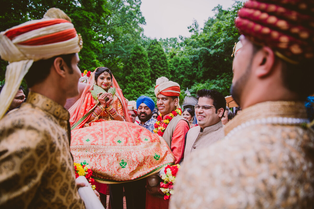 bengali indian bride covering her face with betel leaves circling the groom during hindu saat paak ceremony