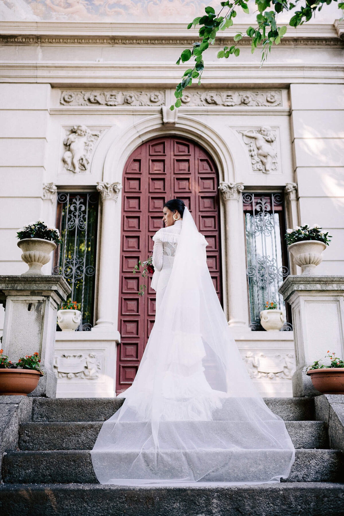 A bride on her back, standing on the top of the stairs, her long veil flowing down the stairs on a vintage villa background