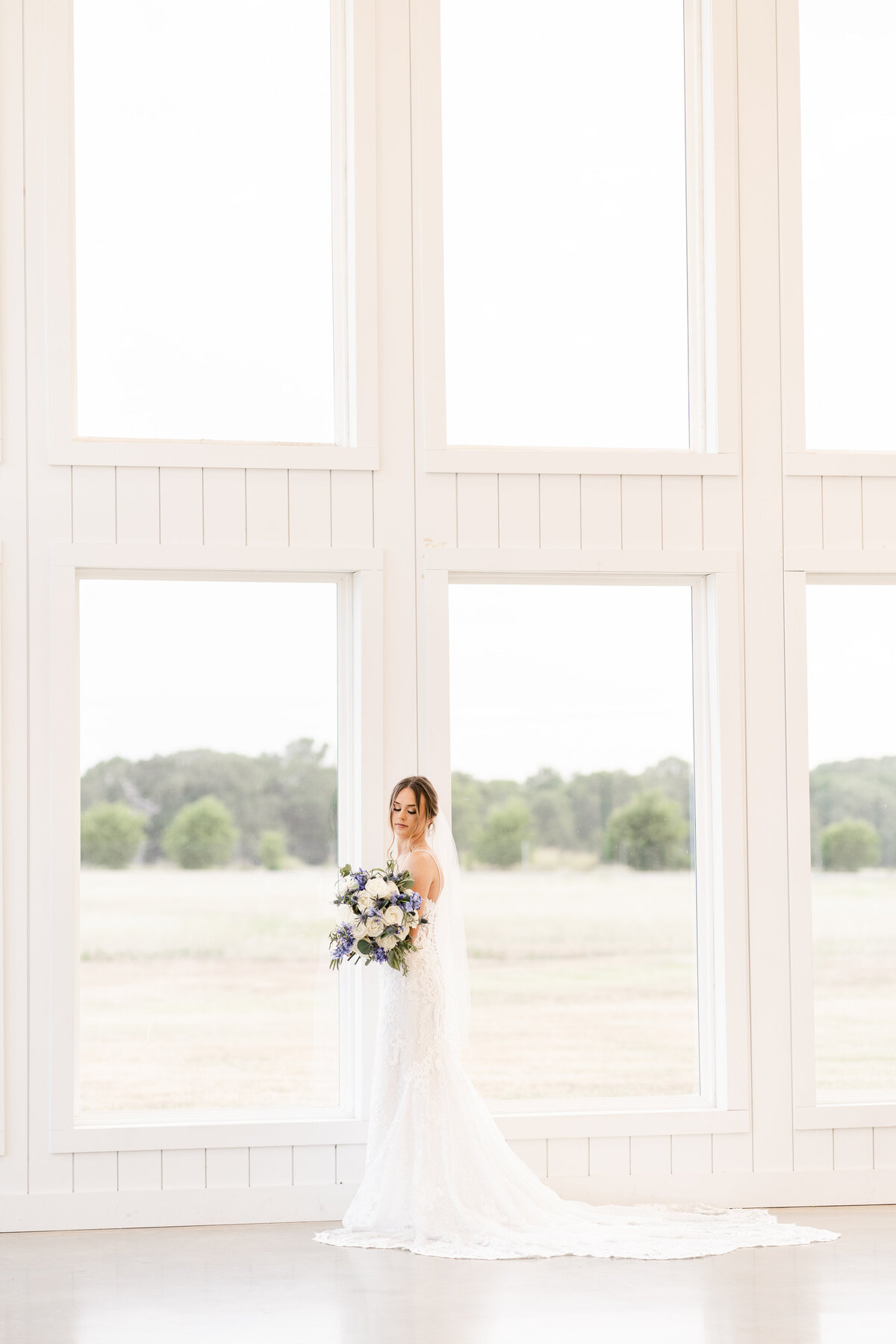 Bride with wedding bouquet and cathedral veil in an all white venue at The Ranch House