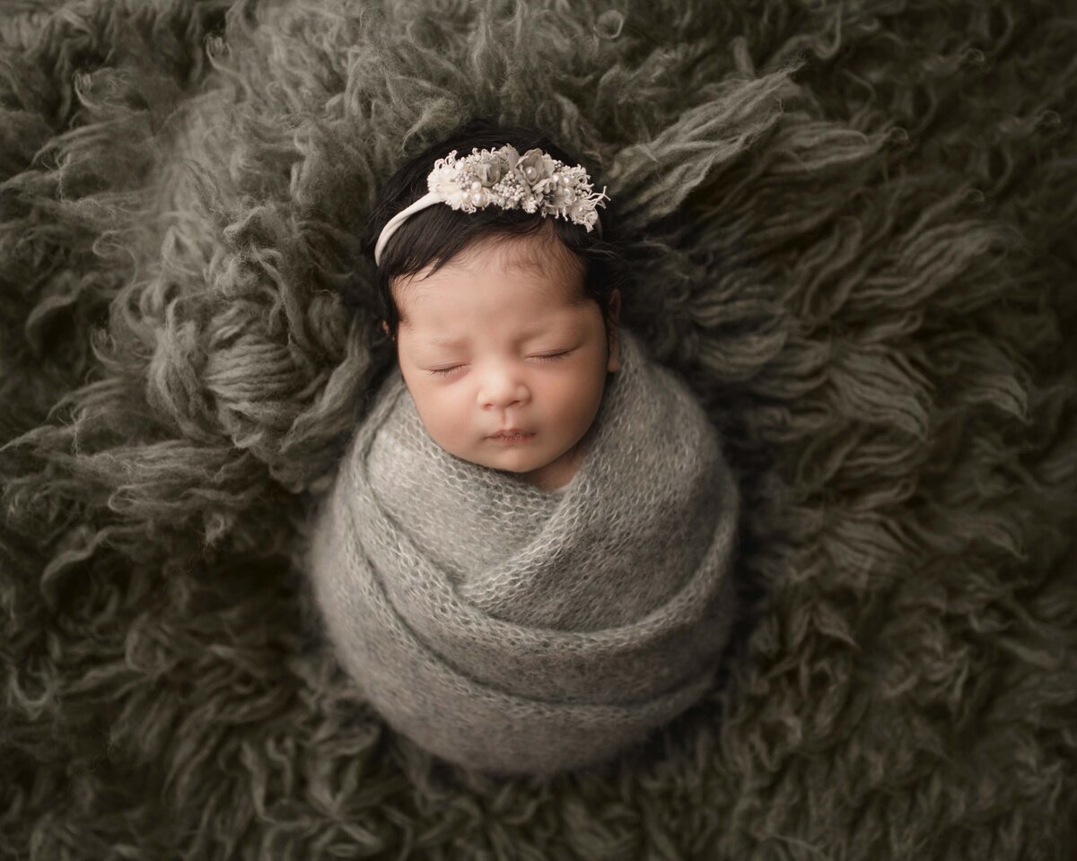 Aerial image. Lake Elsinore newborn photoshoot. Baby girl is swaddled in olive knit wrap with a sage headband. Baby is sleeping peacefully. Captured by best Lake Elsinore newborn photographer Bonny Lynn Photography.