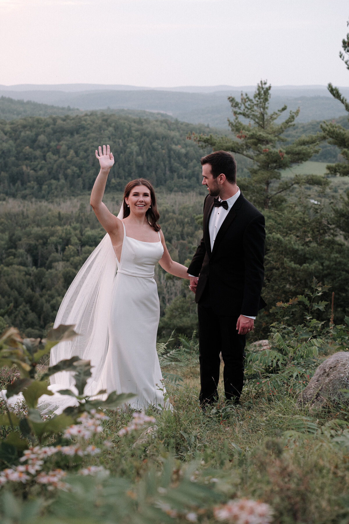 bride waving at their guests while the groom is in awe of her beauty