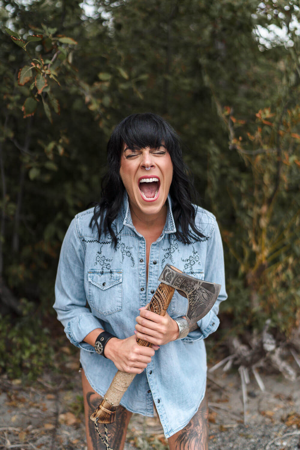 expressive woman yelling with eyes closed and holding a tomahawk in outdoor setting